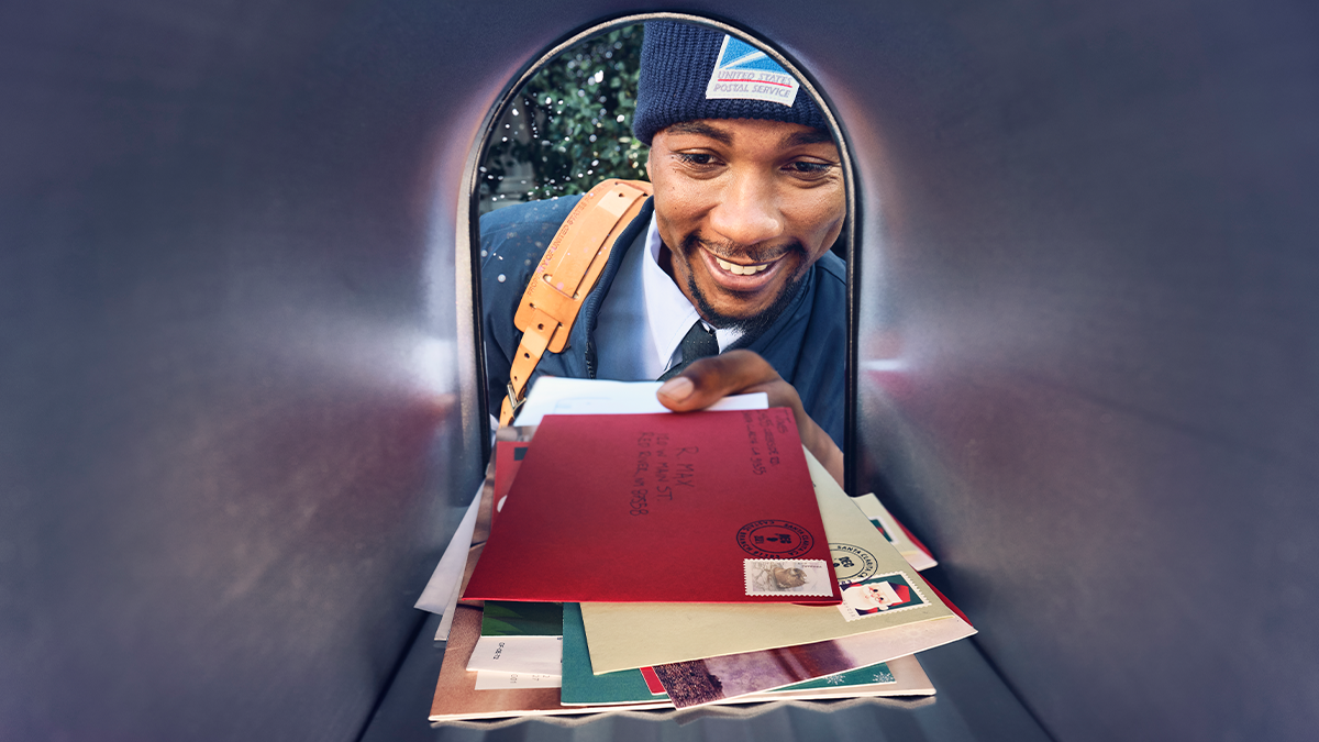 View from inside a mailbox of mail carrier putting a stack of letters into the mailbox.